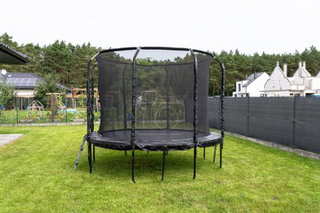 Grand trampoline pour enfants avec filet de protection et fermeture éclair fermée, debout dans le jardin, maille visible masquant la clôture.