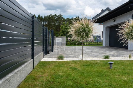 A modern panel fence in anthracite color, visible sliding gate to the garage and a garbage place in the corner.