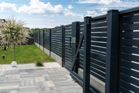 Téléchargez les photos : A modern panel fence in anthracite color, a visible sliding gate to the garage and a wicket with a letterbox. - en image libre de droit