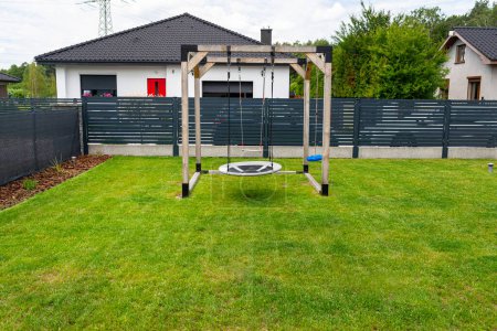 Une aire de jeux moderne en bois de forme carrée, faite de coins métalliques, debout sur la pelouse dans la cour.