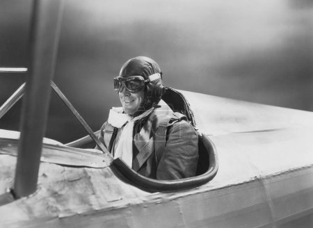 Smiling male pilot in goggles and cap flying airplane 