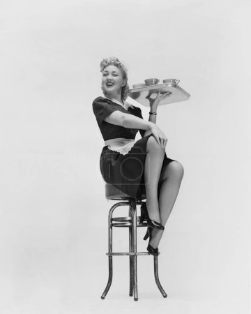 Foto de Longitud completa de joven camarera sonriente con bandeja sentada en el taburete - Imagen libre de derechos