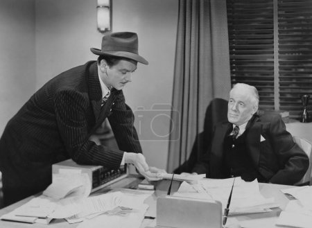 Foto de Jefe mirando a hombre de negocios con sombrero compartiendo documento en la oficina - Imagen libre de derechos