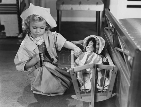 Foto de Chica imitando como médico comprobar el tiempo mientras toma de la mano de la muñeca en la cuna - Imagen libre de derechos