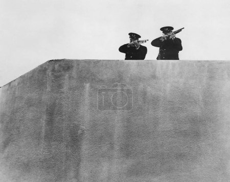 Foto de Vista de ángulo bajo de los oficiales apuntando rifles mientras están de pie en la terraza contra el cielo - Imagen libre de derechos