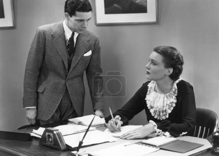 Foto de Empresario mirando a secretaria que escribe en papel mientras que trabaja en oficina - Imagen libre de derechos
