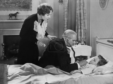 Foto de Médico varón examinando al niño enfermo acostado en la cama con estetoscopio en casa - Imagen libre de derechos
