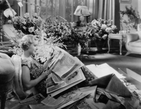 Téléchargez les photos : Vue latérale de la femme coupant des photos du journal tout en étant assis sur le canapé dans l'appartement - en image libre de droit