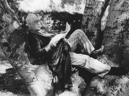Foto de Vista lateral de cuerpo entero del hombre maduro recostado en el árbol mientras lee el periódico - Imagen libre de derechos
