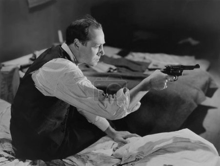 Foto de Vista lateral del hombre alerta con pistola sentado en la cama en casa - Imagen libre de derechos