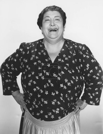 Foto de Feliz mujer de gran tamaño riendo mientras está de pie con los brazos akimbo contra la pared - Imagen libre de derechos
