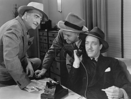 Foto de Curiosos hombres de negocios tratando de escuchar a su colega hablando por teléfono en la oficina - Imagen libre de derechos