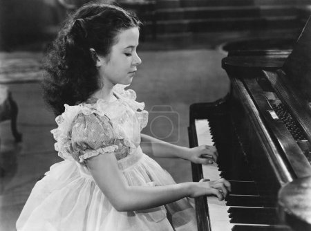 Foto de Adolescente en vestido tocando piano de cola en casa - Imagen libre de derechos