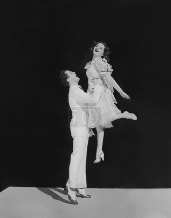 Foto de Vista lateral de un joven recogiendo a una mujer feliz mientras está de pie sobre un fondo negro - Imagen libre de derechos