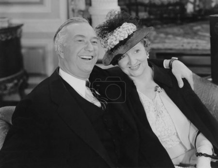 Foto de Feliz hombre mayor con el brazo alrededor de la mujer usando sombrero mientras está sentado en el sofá - Imagen libre de derechos