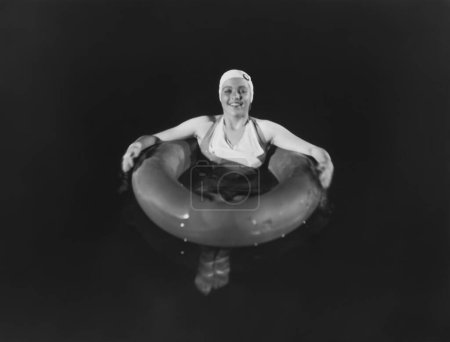 Foto de Retrato de mujer sonriente flotando con tubo en piscina por la noche - Imagen libre de derechos