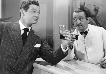 Foto de Hombre y camarero tostando bebidas en el mostrador en el bar - Imagen libre de derechos