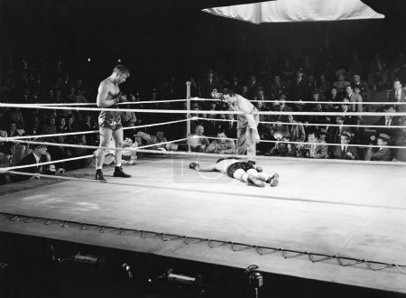 Foto de Árbitro cuenta atrás nocaut en el ring de boxeo rodeado de audiencia - Imagen libre de derechos