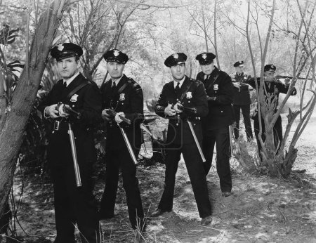 Foto de Equipo de policías masculinos apuntando con armas mientras están de pie en medio de árboles en el bosque - Imagen libre de derechos