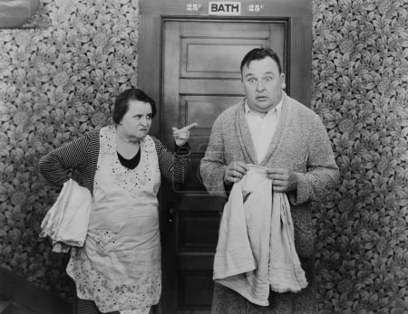 Foto de Mujer agresiva casera señalando sorprendido inquilino masculino de pie con toalla baño exterior - Imagen libre de derechos