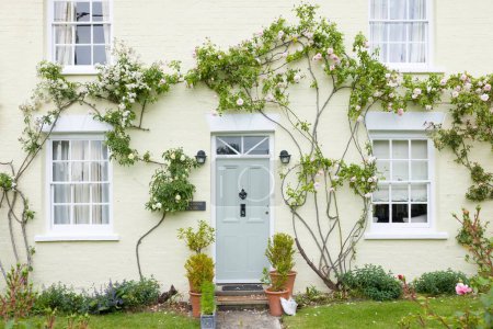 Photo for BUCKINGHAMSHIRE, UK - June 03, 2022. Home exterior UK. English house with green front door and wooden sash windows surrounded by climbing roses. England, UK - Royalty Free Image