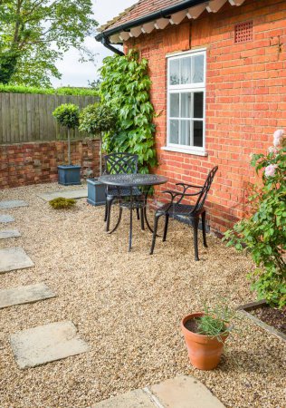 UK garden patio design. Hard landscaping with York stone stepping stones in gravel and a metal bistro table and chairs.