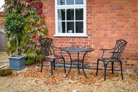 Téléchargez les photos : Jardin paysager dur en automne avec meubles de jardin patio. Gravier avec une table de bistrot en métal noir et des chaises. - en image libre de droit