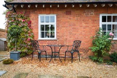 Téléchargez les photos : Jardin paysager dur en automne avec meubles de jardin patio. Gravier et pierre de York avec une table de bistrot en métal noir et des chaises. - en image libre de droit
