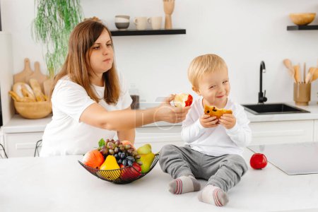 Foto de Mamá hace que el niño coma bien. Mamá está tratando de enseñarle a su hijo a comer saludablemente. Disfrutar de alimentos a base de plantas - Imagen libre de derechos