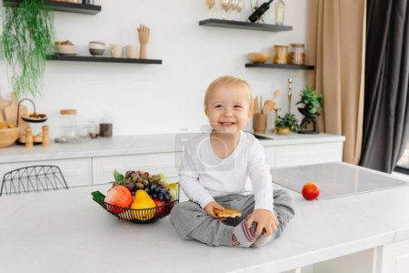 Foto de Un niño feliz sentado en la cocina sonriendo junto a frutas y verduras. - Imagen libre de derechos