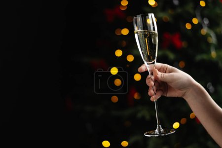 Téléchargez les photos : Une main de femme avec une coupe de champagne sur fond de lumières de Noël. - en image libre de droit
