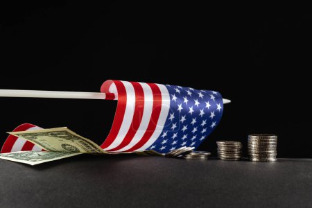 Photo for The concept of the decline of the U.S. economy. American flag fallen lies on black background next to US dollars and coins. - Royalty Free Image
