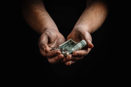 Photo for The dirty hands of a homeless man, a poor man holding not much money, dollars. The concept of helping homeless and underprivileged people. Conceptual image of dirty hands holding a few dollars - Royalty Free Image