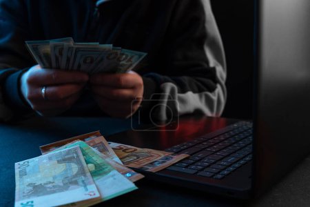 Foto de A man counts the money in front of his laptop. The concept of making money on the Internet. - Imagen libre de derechos