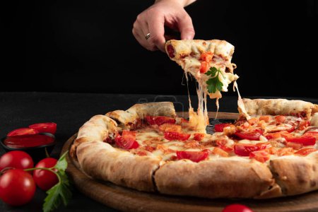 Photo for Margarita pizza. A mans hand takes a slice of pizza with a spatula, the cheese on the pizza stretches. - Royalty Free Image