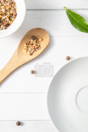 Foto de Varias especias en una cuchara de madera sobre fondo de madera blanca con otros utensilios de cocina blancos y hojas verdes. Foto de alta calidad - Imagen libre de derechos