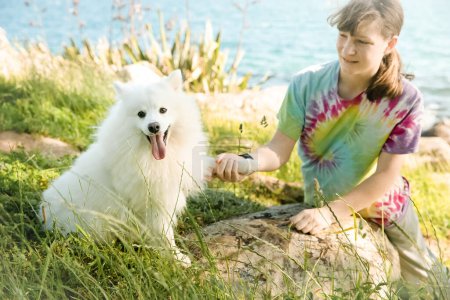 Foto de Caucasian happy girl with a white fluffy dog on natural background, outdoors. High quality photo - Imagen libre de derechos