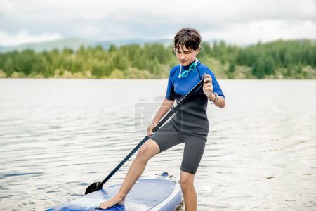 Téléchargez les photos : Active teen girl paddling a sup board on a river or lake, natural background, active healthy sporty lifestyle. High quality photo - en image libre de droit