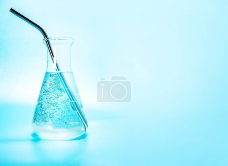 Téléchargez les photos : Liquide clair avec des bulles d'eau dans une fiole de laboratoire en verre, bouteille isoaltérée sur fond bleu. Photo de haute qualité - en image libre de droit