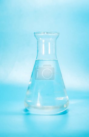 Téléchargez les photos : Liquide clair avec des bulles d'eau dans une fiole de laboratoire en verre, bouteille isoaltérée sur fond bleu. Photo de haute qualité - en image libre de droit