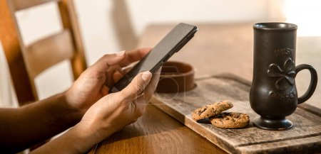 Photo for Hands holding phone, oatmeal cookies and cup for irish coffee in the background. - Royalty Free Image