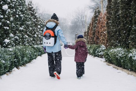 Photo for Happy Family, mother, son and cat in backpack walking on the snowy alley in winter snowy nature background. Mom, kid boy having fun, running, playing snow ball together outdoors at winter park. - Royalty Free Image