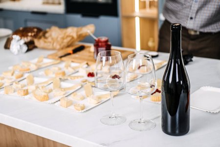 Photo for Wine Tasting Preparation with Cheese Pairings. Sommelier prepares for a wine tasting event, carefully pairing various cheeses with wines, featuring an unopened bottle and elegant glasses - Royalty Free Image