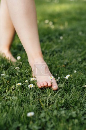 Sobreestimulación: Cómo manejar la sobrecarga sensorial. Un primer plano de pie desnudo tocando hierba verde con delicada flor de margarita, momento de conexión con la naturaleza para contrarrestar la sobrecarga sensorial