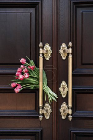 Welcome and Hospitality. Tulips bouquet Beside Ornate Wooden Door Welcome Symbol. The flowers next to a door symbolize a warm welcome or hospitality in home or upscale venue