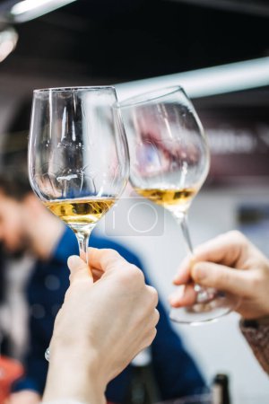 Two wine enthusiasts engage in the sensory experience of wine tasting, assessing the quality of a golden wine at a trade fair.