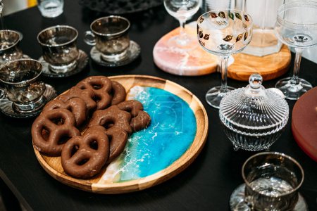 Ein raffinierter Brotaufstrich mit Gourmetschokolade überzogenen Brezeln auf einem handgefertigten Servierbrett aus Holz und Harz mit feinen Gläsern.