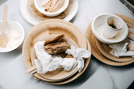 Used biodegradable plates and wooden utensils on a table, highlighting the eco-friendly choice for disposable tableware after a meal.