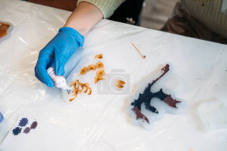 Close-up of a persons hands wearing gloves, meticulously adding pigments to an epoxy resin art piece in a workshop setting.