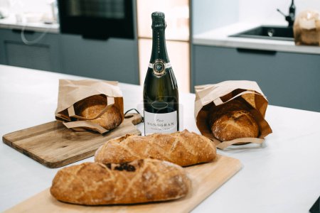 Téléchargez les photos : Une bouteille de Franciacorta Brut élégamment affichée avec du pain artisanal fraîchement cuit sur un comptoir de cuisine. - en image libre de droit